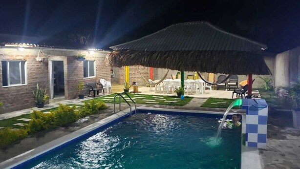 An outdoor swimming pool area with a thatched roof, lounge chairs, and a small garden. - Cabaña el Eden is an ideal place for family relaxation. (Santa Verónica)