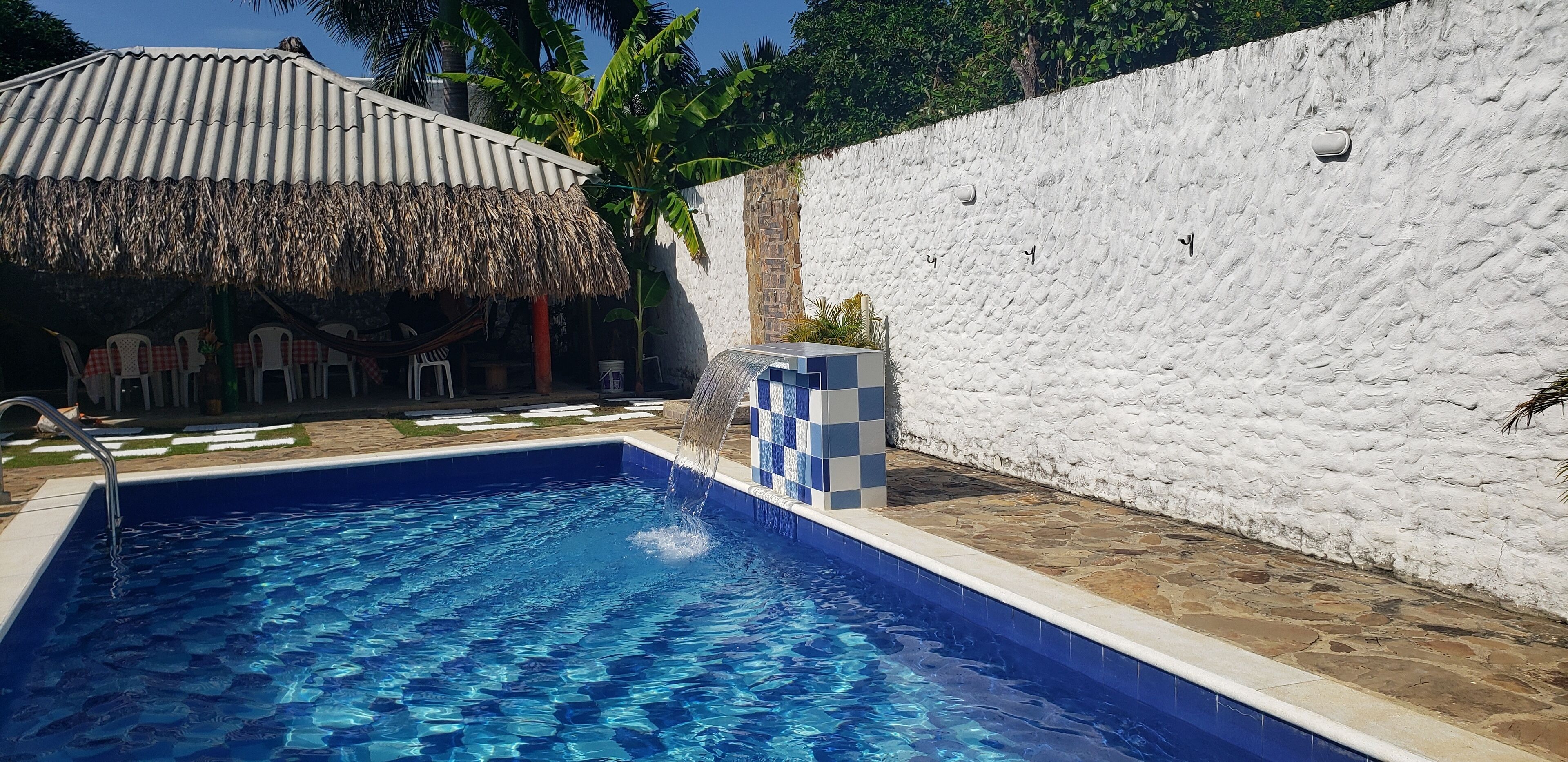 A swimming pool with a thatched roof structure and white stone walls.