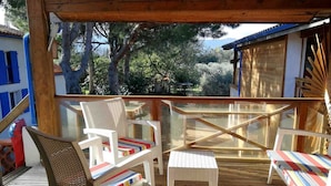 A wooden deck with two wicker chairs and a small table, overlooking a scenic landscape with trees and a building in the background. - Miro - ARGELES-SUR-MER (ARGELES-SUR-MER)