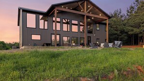 A modern, multi-story building with large windows and a covered outdoor area. - Waterfront 6-Acres w/ Pickleball, Hot Tub, Cold Plunge, Putting Green, Games! (Broken Bow)