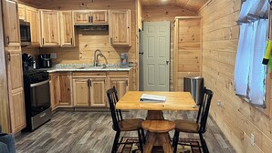 Un intérieur en bois comprenant un espace cuisine avec des armoires en bois, un comptoir en granit, une table à manger avec des chaises et un ventilateur de plafond.