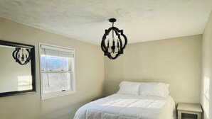 Une chambre à coucher avec un lit, une petite table de chevet, une fenêtre et un lustre.
