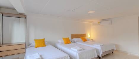 A hotel room with three single beds, a wooden desk, and a mirror.