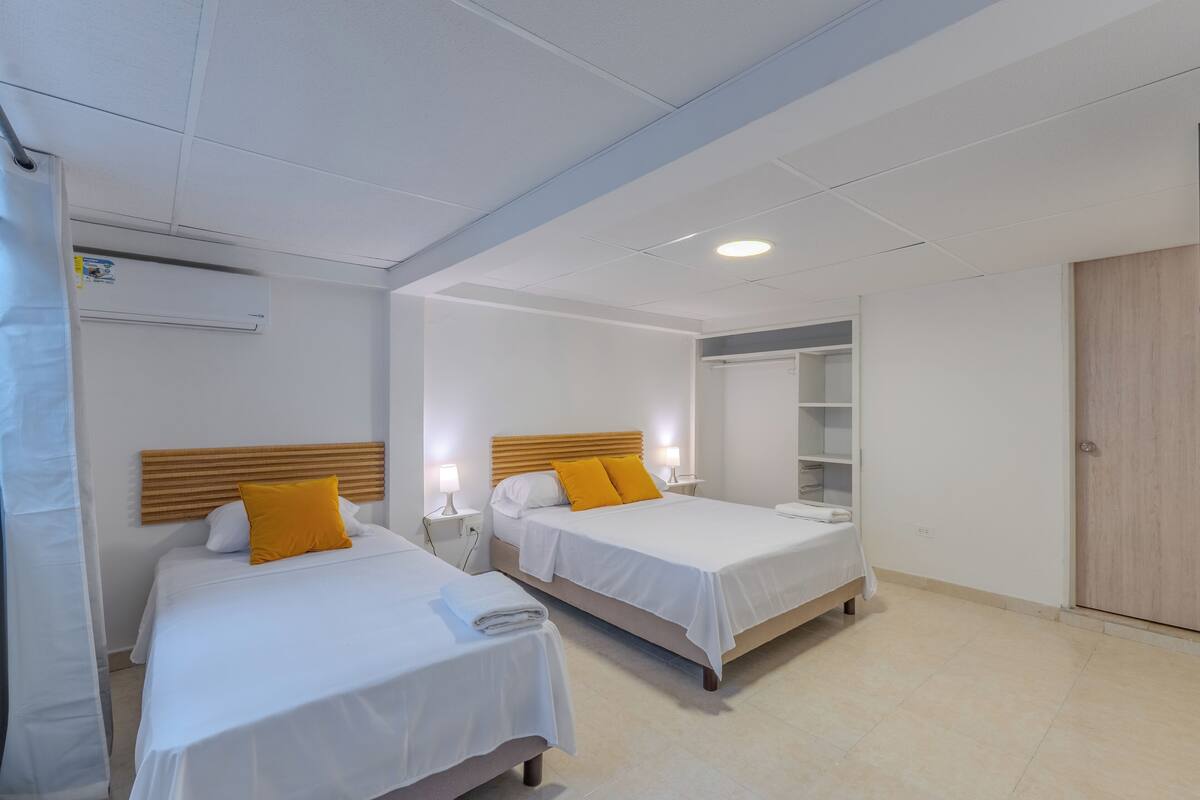 A hotel room with two beds, a wooden headboard, a mirror, a wardrobe, and an air conditioning unit.