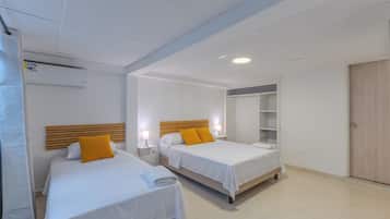 A hotel room with two beds, a wooden headboard, a mirror, a wardrobe, and an air conditioning unit.