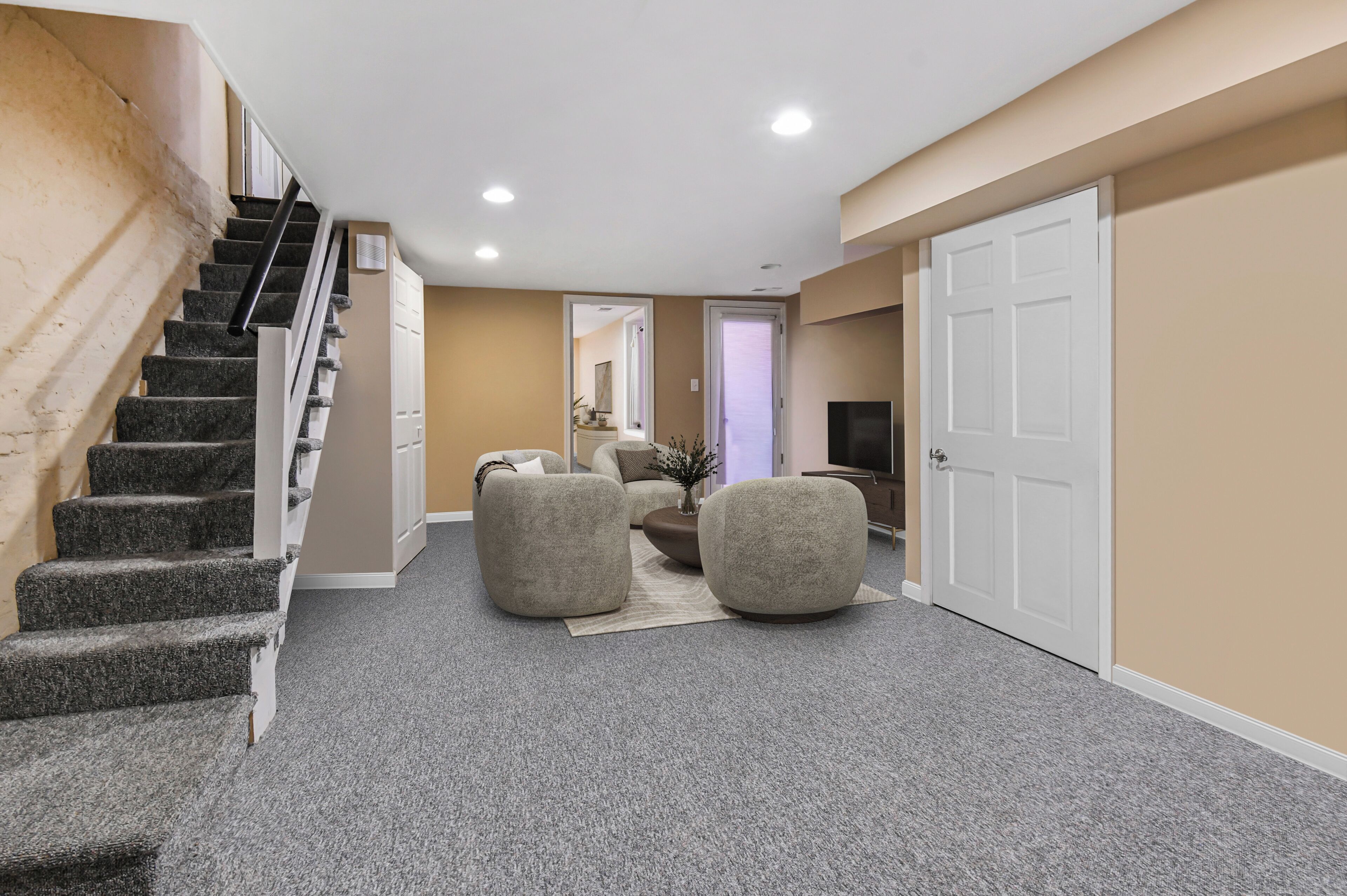 A spacious hallway with a carpeted floor, a staircase, and a door leading to another room.
