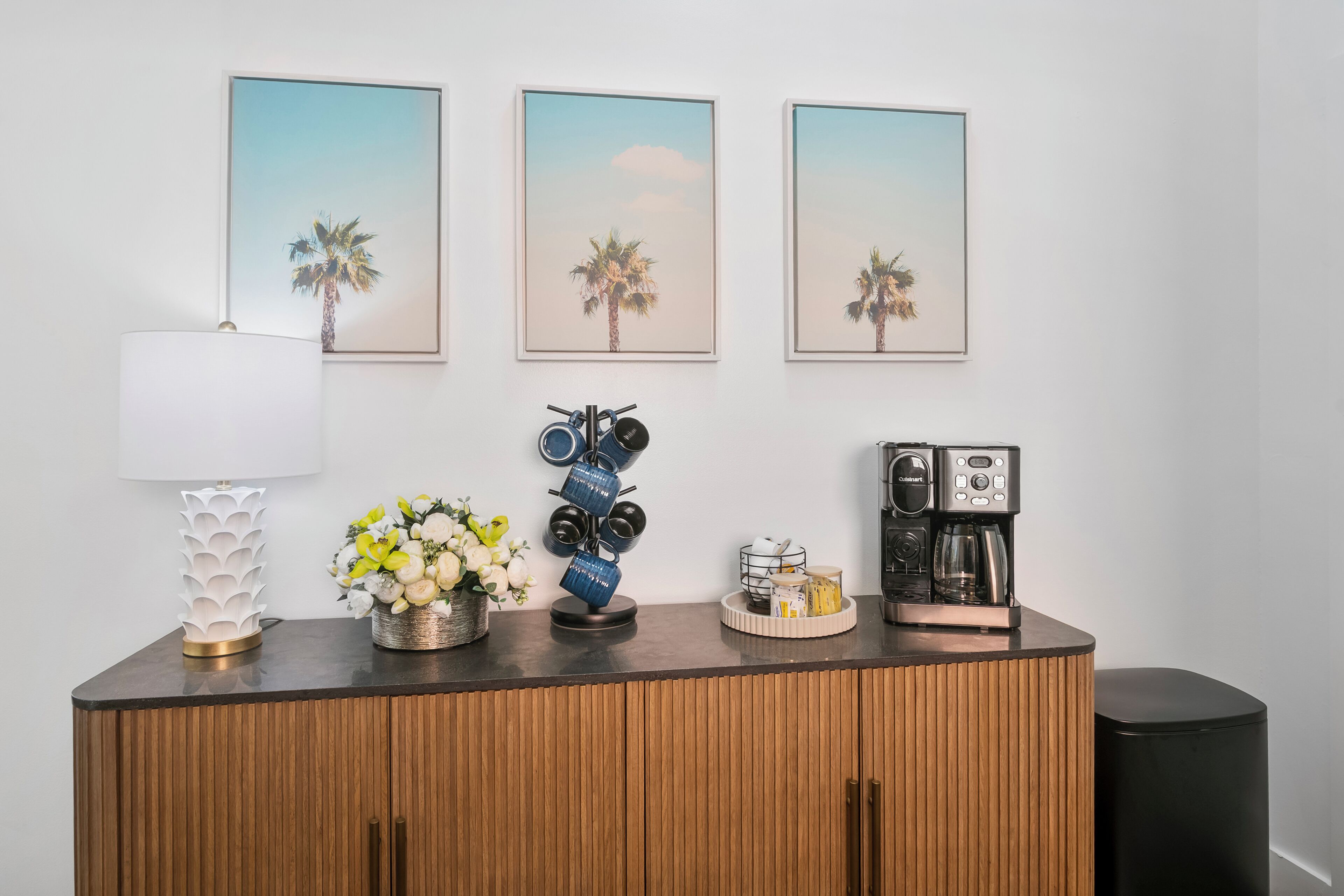 A wooden cabinet with a coffee maker, a lamp, and a vase of flowers.