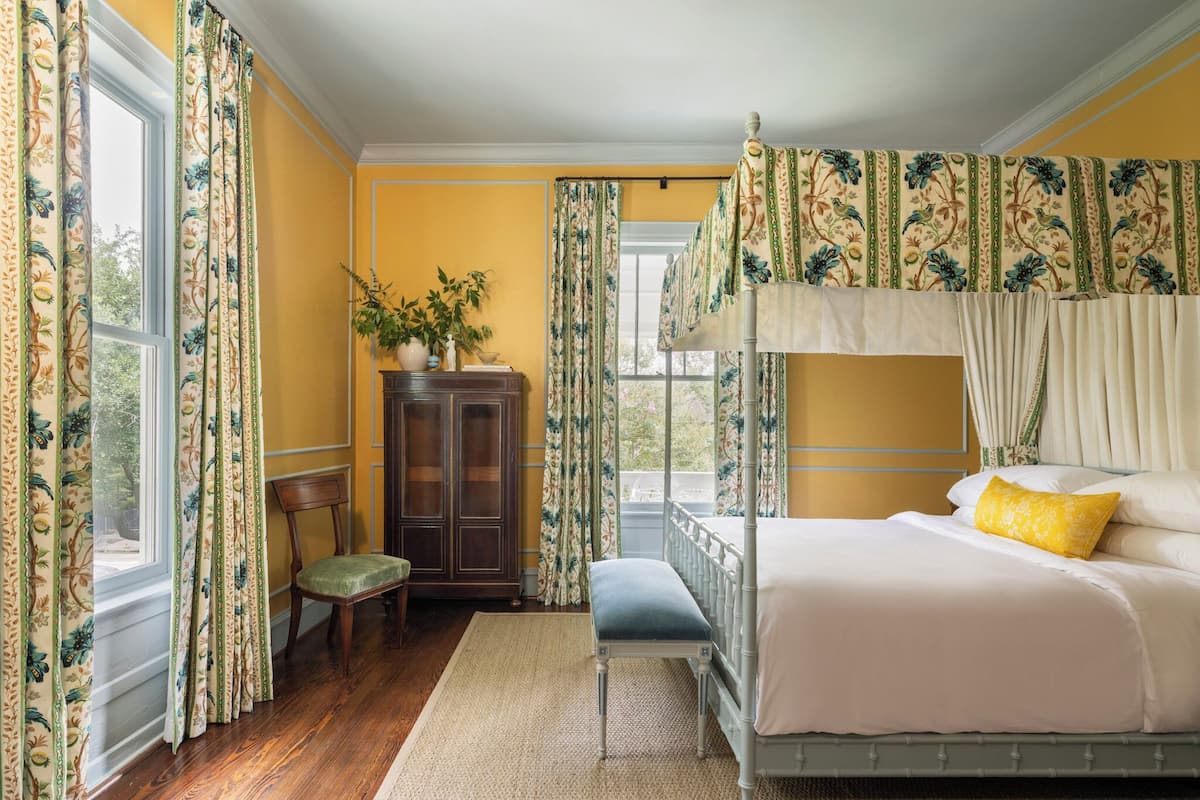Un dormitorio con cama con dosel, un aparador de madera, una silla y una ventana con cortinas.