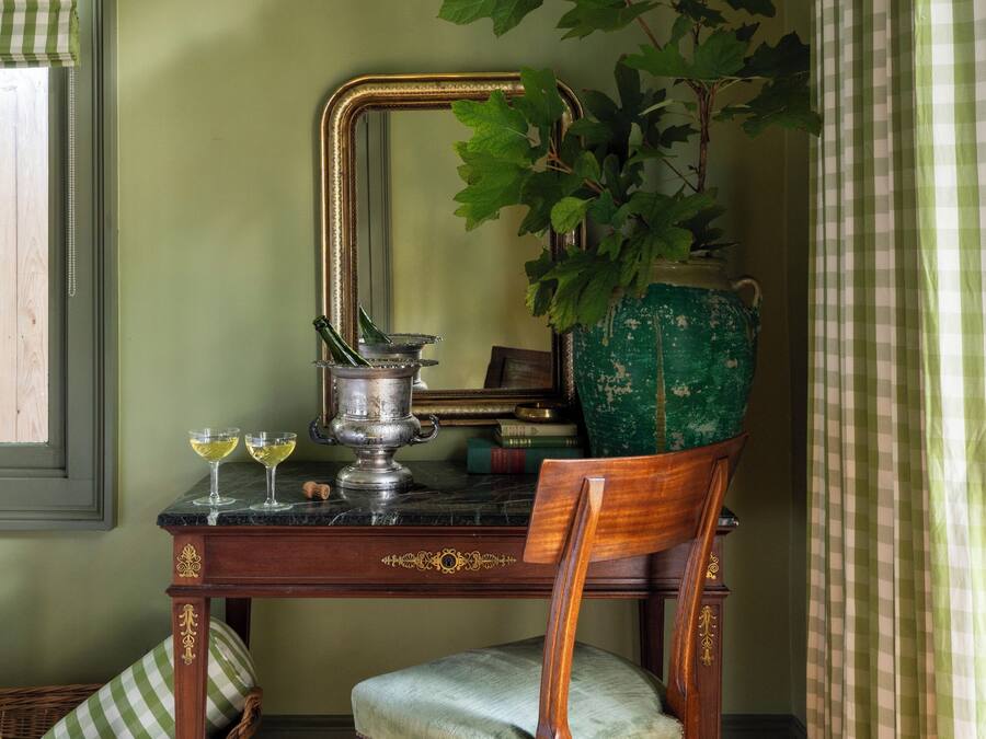 A room with a wooden chair, a green plant in a pot, a metal container, and a checkered curtain.