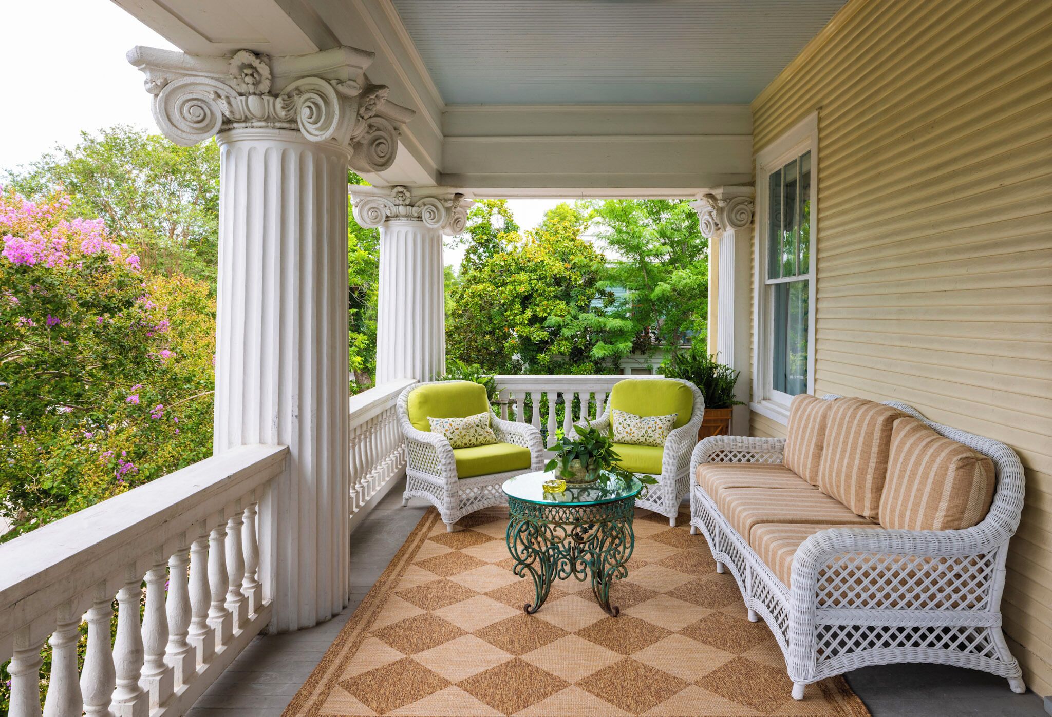 A porch with white wicker furniture, a glass table, and a checkered floor.