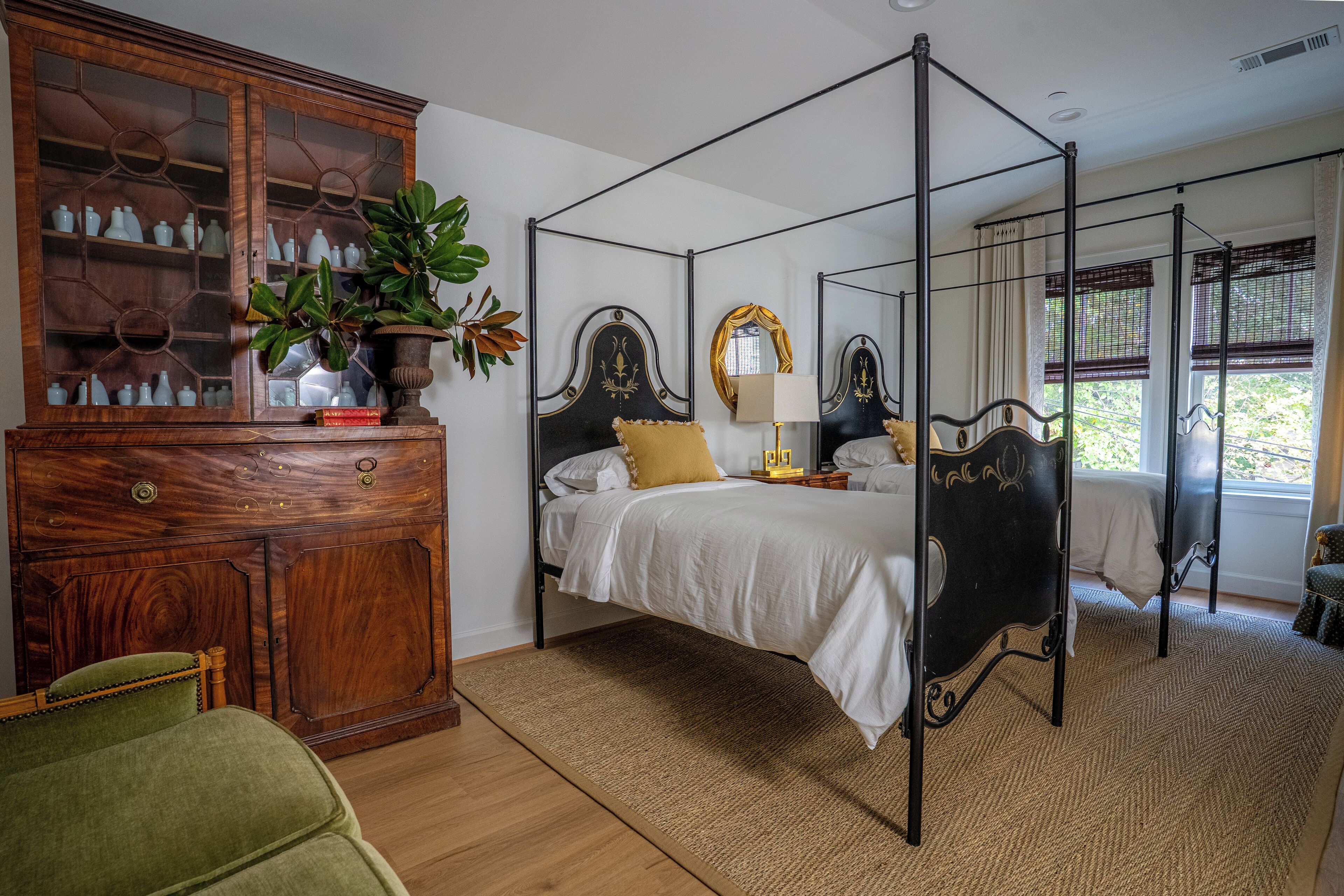 A four-poster bed with a wooden headboard, a green armchair, and a wooden cabinet with glass doors.