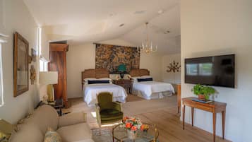 Una habitación amplia con una cama grande, un sillón verde, una mesa de centro con flores y un televisor en la pared.