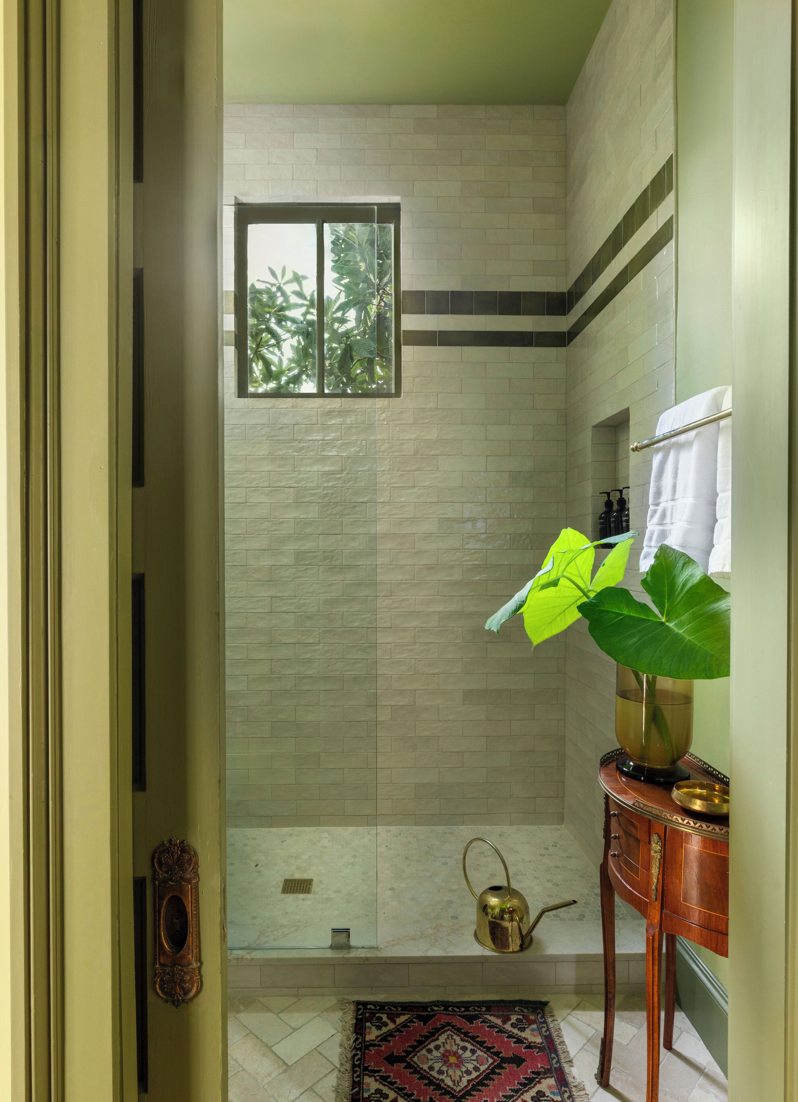 A bathroom with a shower, a window, a sink, and a decorative plant.