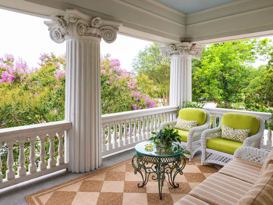 A covered porch with white columns, a checkered floor, and a green and white wicker sofa.