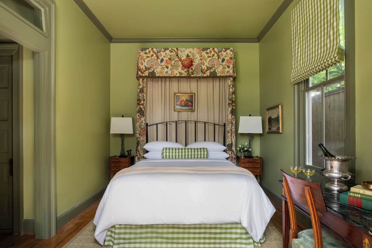Un dormitorio ordenado con una cama grande, dos mesitas de noche con lámparas, una silla y una ventana con cortinas.
