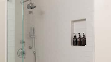 A glass-enclosed shower with a white tiled wall, a small shelf with toiletries, and a hexagonal patterned floor.