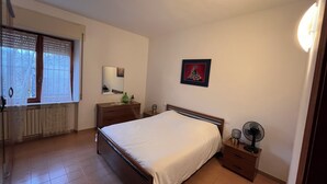 A bedroom with a bed, a dresser, a bedside table with a fan, a window with blinds, and a mirror. - Casa Rina Family home apartment. Umbria / Tuscany. 2 minutes from the lake (Umbria)