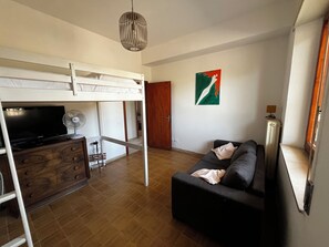 Un salon avec un canapé, un téléviseur, un ventilateur, un lit superposé et une porte.