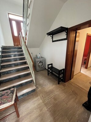 Een trap met houten leuning, een wasmachine en een bank in een woonkamer.
