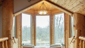 Ein Holzblockhaus-Interieur mit hoher Decke, großen Fenstern, zwei Stühlen und einem Teppichboden.