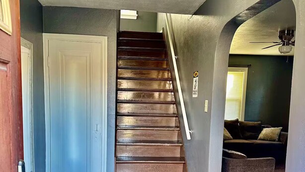 A staircase with wooden steps leading to a landing, a door on the left, and a couch in the background. - single family home, easy access, safe area (South Bend)