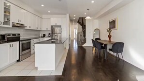 A modern kitchen with white cabinetry, a central island, and a dining area with a table and chairs. - Serenity Home in Brampton (Brampton)