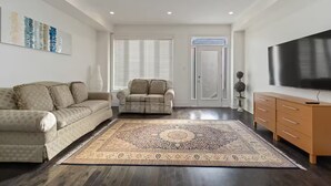A modern living room with a sofa, armchair, and a large flat-screen TV. - Serenity Home in Brampton (Brampton)