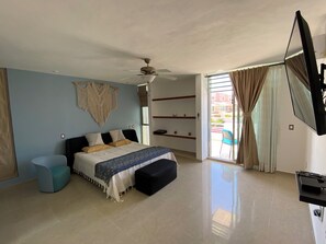 Ein Schlafzimmer mit einem Bett, einem Deckenventilator, einer Wanddeko aus Makramee, einem kleinen Tisch, einem Fernseher und einer Schiebetür zum Außenbereich.