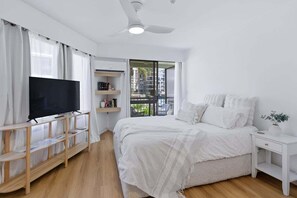 A bedroom with a TV on a wooden stand, a bed with white bedding, a white nightstand, and a ceiling fan. - Surfers Paradise Studio by the Ocean (Gold Coast)