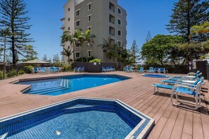 A pool area with two swimming pools, lounge chairs, and a building in the background. - Surfers Paradise Studio by the Ocean (Gold Coast)