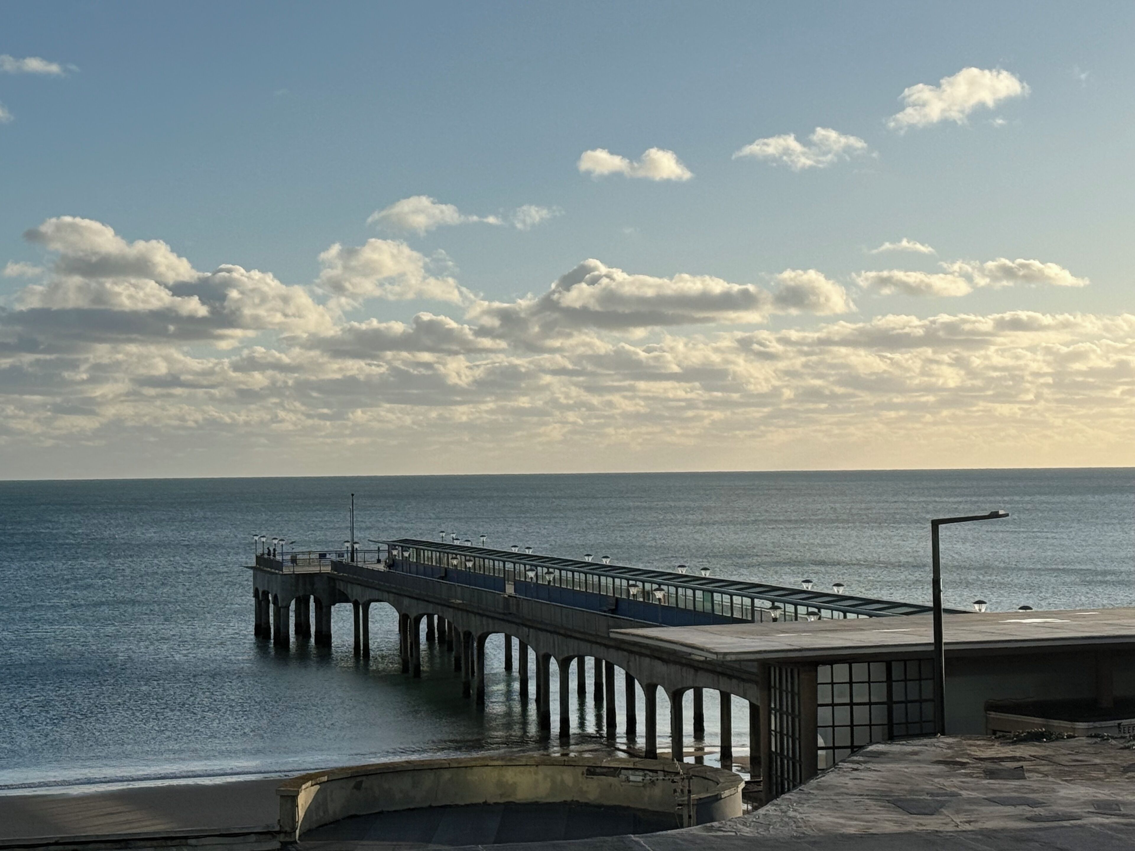 Eine Pier, die sich in ruhiges Wasser erstreckt, mit blauem Himmel darüber.