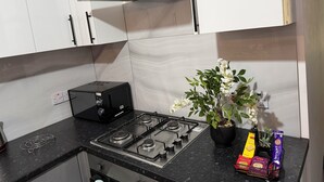 Una cucina con mobili bianchi, un fornello a gas, una cappa aspirante nera e una pianta in vaso.