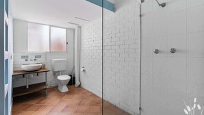 Une salle de bain moderne avec un mur en briques blanches, une douche en verre, des toilettes blanches et un meuble-lavabo en bois avec un lavabo blanc.