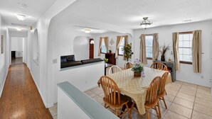 Ein geräumiger Essbereich mit großem Tisch und Stühlen, ein Küchenbereich mit Arbeitsfläche und ein Flur, der zu einem weiteren Zimmer führt.