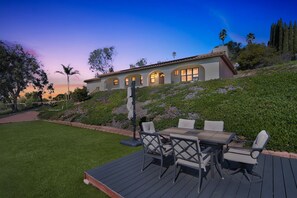 Una casa con un patio attrezzato con tavolo e sedie, circondata da un prato e un giardino curati.