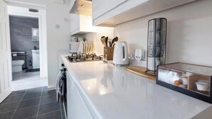 Een moderne keuken met witte kasten, een gasfornuis en een koffiezetapparaat.