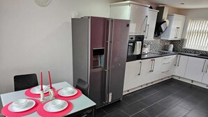 Een moderne keuken met witte kasten, een roestvrijstalen koelkast en een eettafel gedekt met rode placematen.