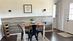 A dining area with a wooden table, black chairs, a rug, and a wall-mounted light fixture.