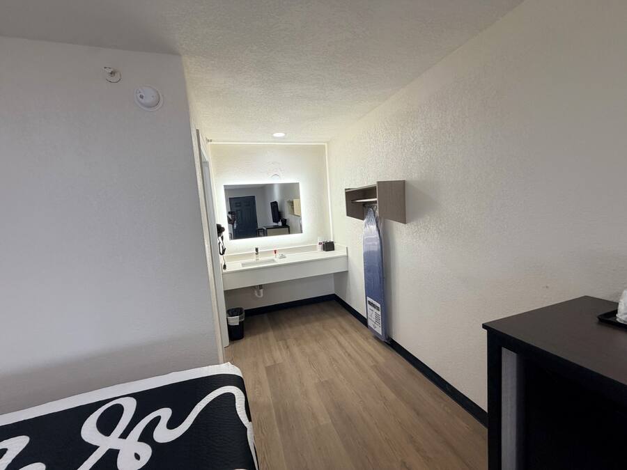 Une chambre d’hôtel avec un plancher en bois, un lavabo blanc, un miroir et une table noire.