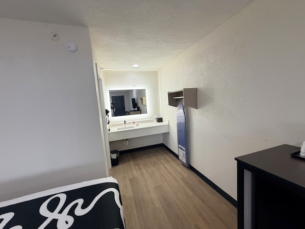 A hotel room with a wooden floor, a white sink, a mirror, and a black table. - Springplace Inn & Suites (Millington)