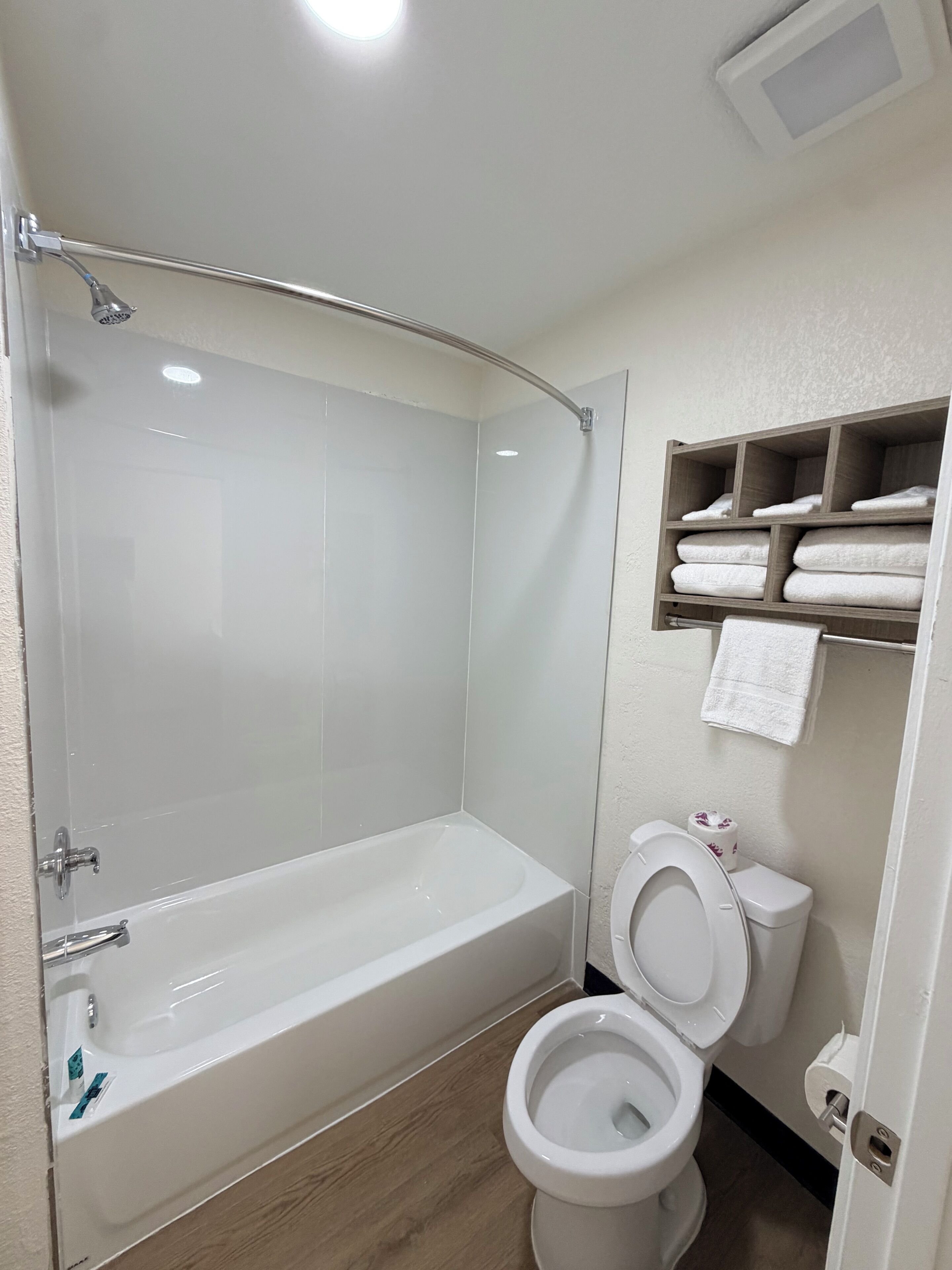 A bathroom with a bathtub, toilet, and a shelf with towels.