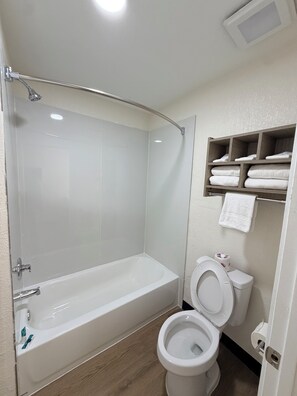 A bathroom with a bathtub, toilet, and a shelf with towels. - Springplace Inn & Suites (Millington)