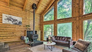 L’intérieur d’une cabane en rondins, avec une cheminée, un canapé en cuir et de grandes fenêtres donnant sur une forêt.