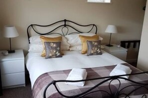 Ein ordentlich bezogenes Bett mit zwei Kissen, einer karierten Decke und zwei Nachttischlampen.