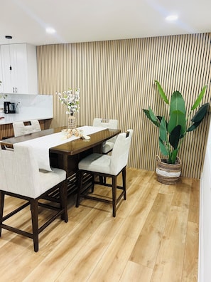 Un espace repas moderne avec une table en bois, des chaises à revêtement blanc et une plante en pot.