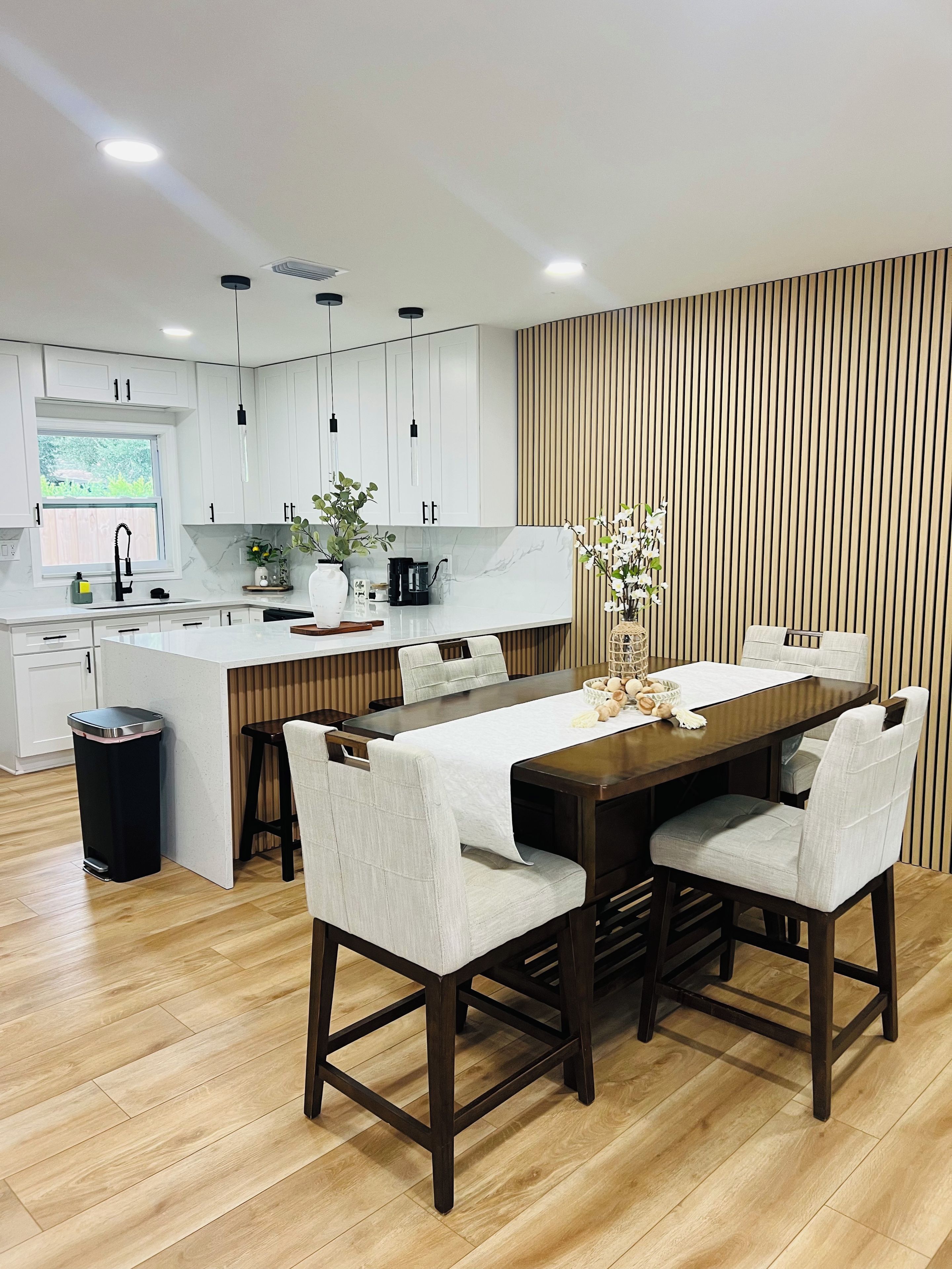 A modern kitchen with white cabinets, a wooden island, and a dining area with a table and chairs.