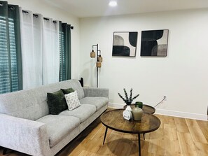 Un salon moderne avec un canapé gris, une table basse ronde en bois et des œuvres d’art abstraites accrochées au mur.