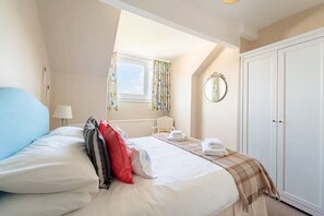 Ein Hotelzimmer mit einem großen Bett, einem Fenster mit Vorhängen, einem Nachttisch mit Lampe, einem Sessel und einem Kleiderschrank.