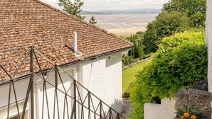 A staircase leading to a white building with a tiled roof, overlooking a beach and greenery. - 2 bedroom self catering apartment with amazing views Chalet studio (Grange-over-Sands)
