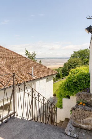 Eine Treppe führt zu einem weißen Gebäude mit einem Ziegeldach, mit Blick auf Strand und Grünflächen.